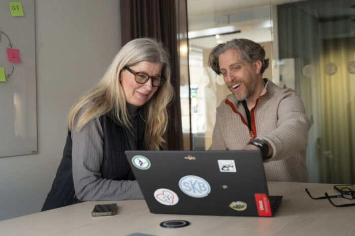 Två glada personer sitter vid en dator och arbetar tillsammans.