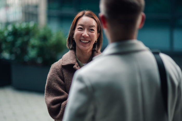 Happy woman smiling while having an outdoor conversation with a man, enjoying a friendly meeting in an urban setting