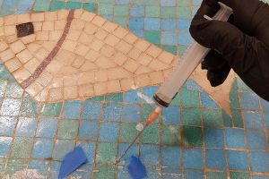 En spruta med nanokalk sticks in i en spricka mellan mosaikplattorna under renoveringen av konstverket.