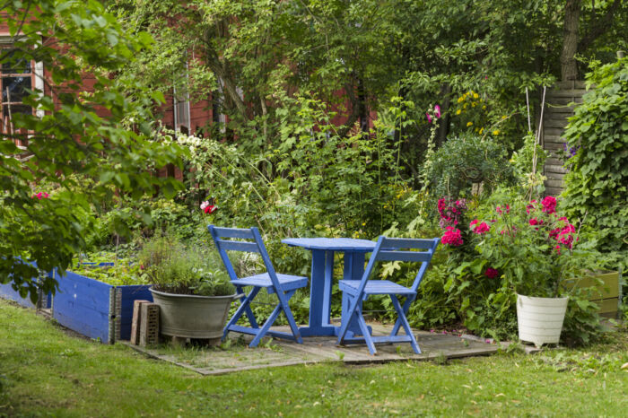 Blå trädgårdsmöbler intill pallkragar med odlade grönsaker och blommor.